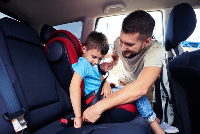 Kindersitzpflicht im Pkw: Vater gurtet seinen Sohn im Autositz an.
