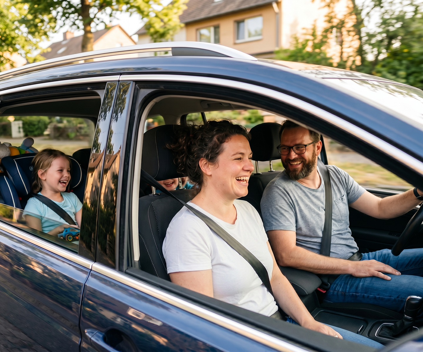 Lachende Familie fährt gemeinsam in einem Auto durch eine Wohnstraße | DA Direkt Vollkaskoversicherung