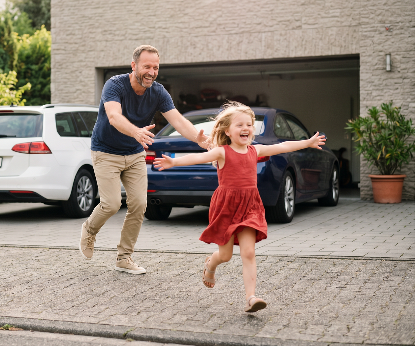 Ein Vater spielt mit seiner Tochter vor der Doppelgarage mit den Familienautos | DA Direkt Zweitwagenversicherung