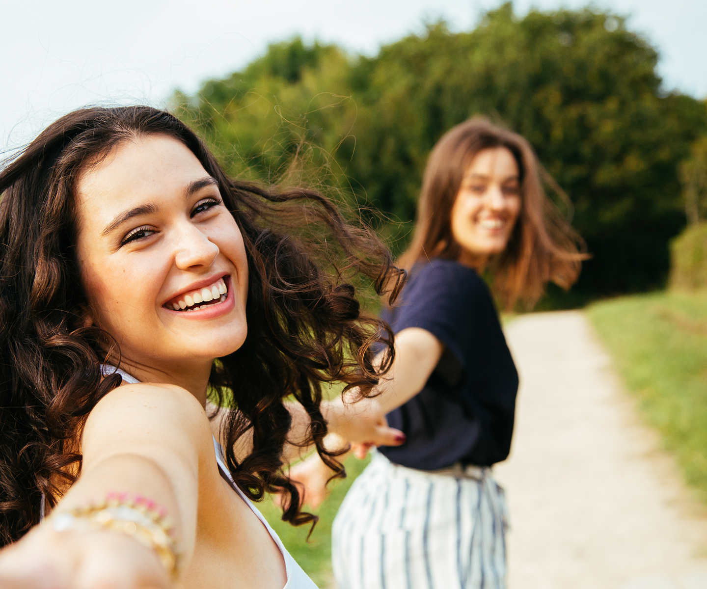Zwei Frauen beim gemeinsamen Spaziergang im Grünen; sie lachen beide.